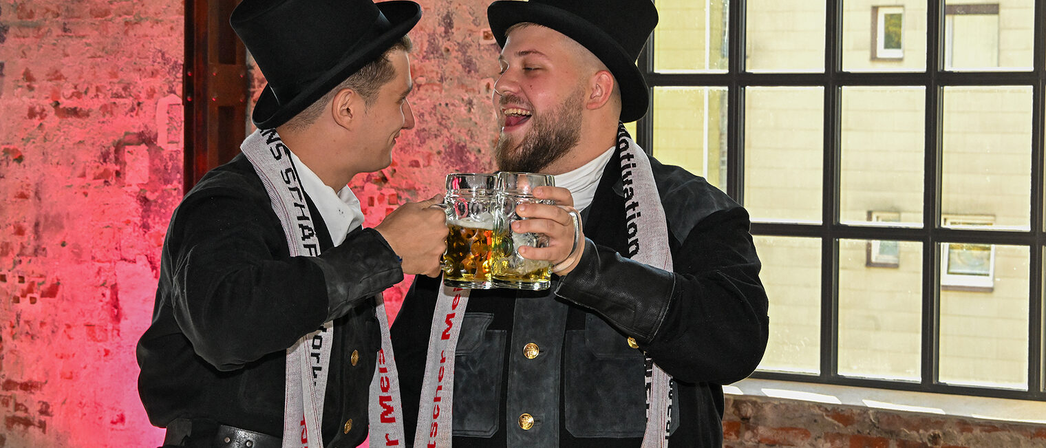 Zwei Schornsteinfegermeister stoßen mit Bierkrügen an.