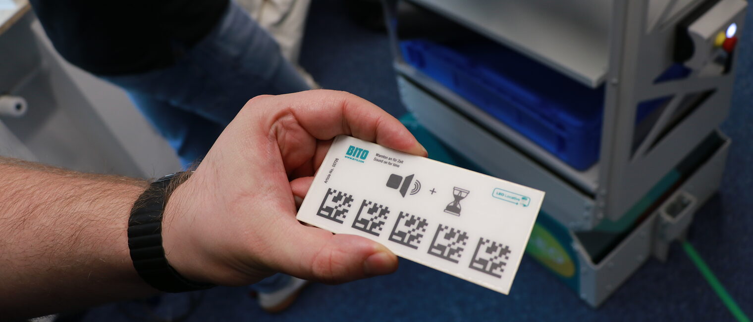 Eine Person hält eine QR-Code-Karte für den Serviceroboter in der Hand.