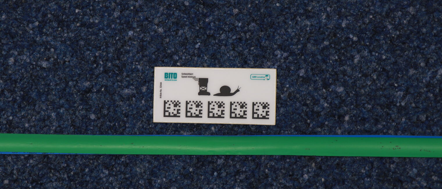 QR-Code-Karte mit Anweisungen für den Serviceroboter neben der Spurbahn