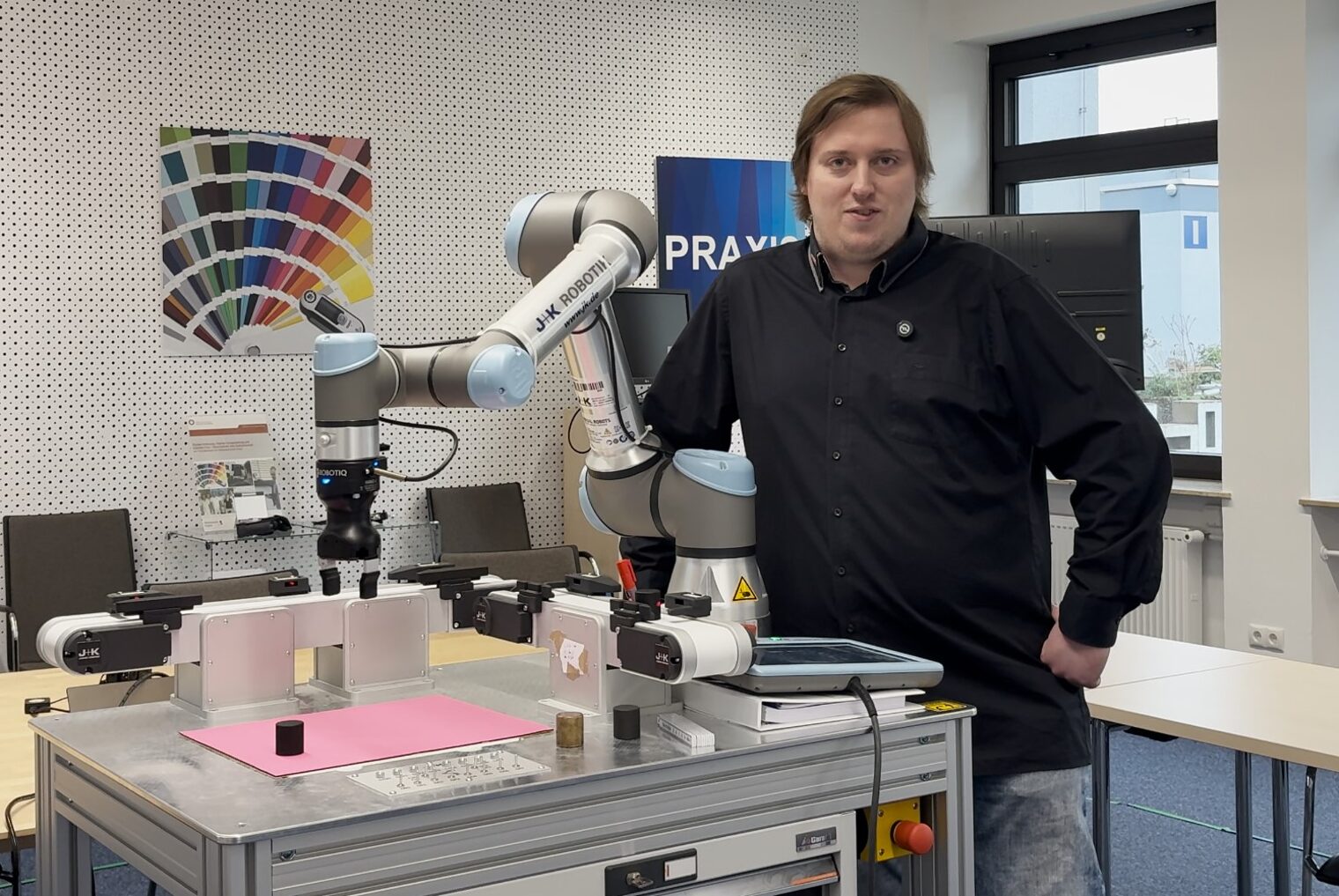 KI-Trainer Robert Falkenstein steht neben dem Roboterarm.