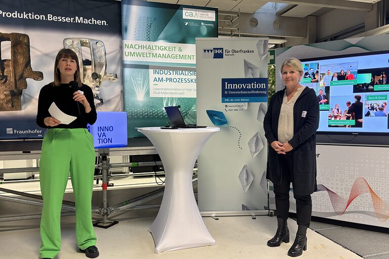 Annegret Schnick moderiert am Mikrofon neben Dr. Petra Beermann im Keylab Additive Innovationen der Uni Bayreuth.