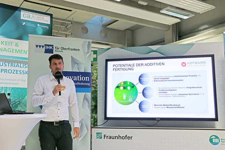 Doktor Andreas Hofmann spricht neben seiner Präsentation auf dem Bildschirm in ein Mikrofon.