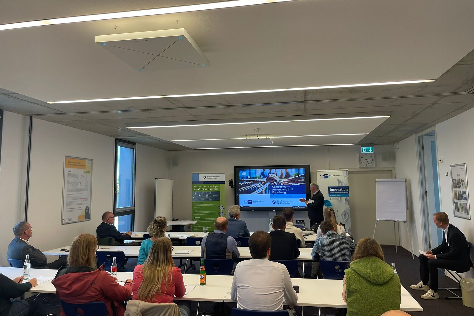 Die Zuhöhrerinnen und Zuhöhrer sitzen in einem Veranstaltungsraum und folgen dem Vortrag von Doktor Waasner.