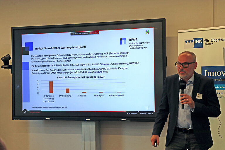 Professor Günter Müller-Czygan spricht neben einer Statistik auf einer Präsentationsfolie ins Mikrofon.