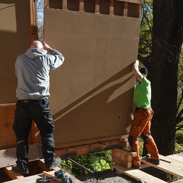 Zwei Männer montieren eine Hauswand aus Holz.