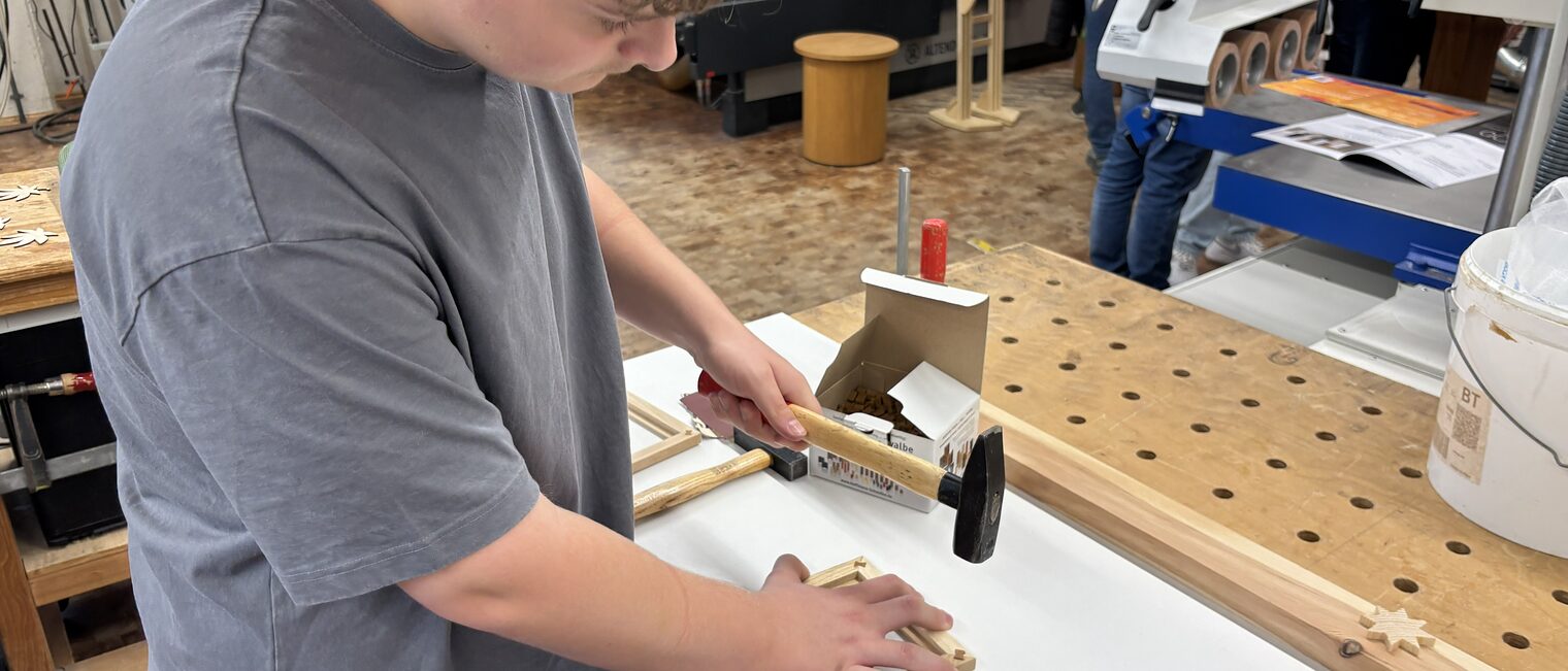Ein Jugendlicher hämmert einen Bildrahmen aus Holz zusammen.