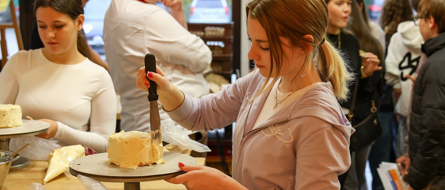 Eine Jugendliche trägt Buttercreme auf eine Torte auf. 