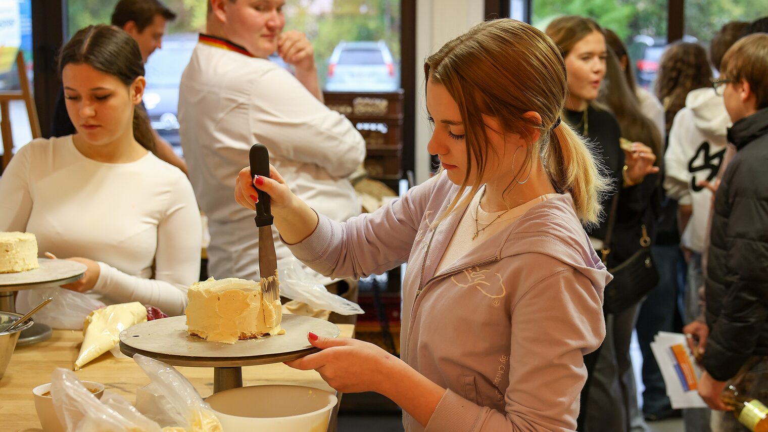 Eine Jugendliche trägt Buttercreme auf eine Torte auf. 