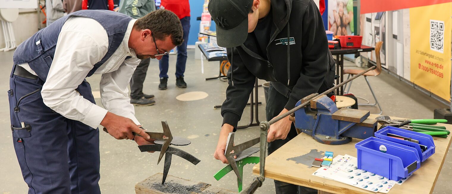Ein Dachdecker zeigt einem Jugendlichen, wie er ein Dekoherz aus Schieferplatten herstellt.