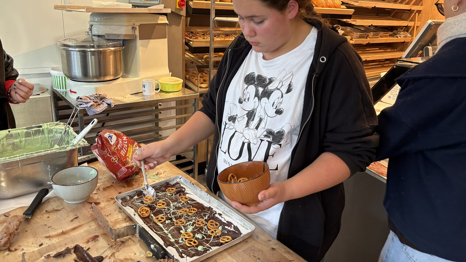 Eine Jugendliche garniert Bruchschokolade mit kleinen Salzbretzeln.