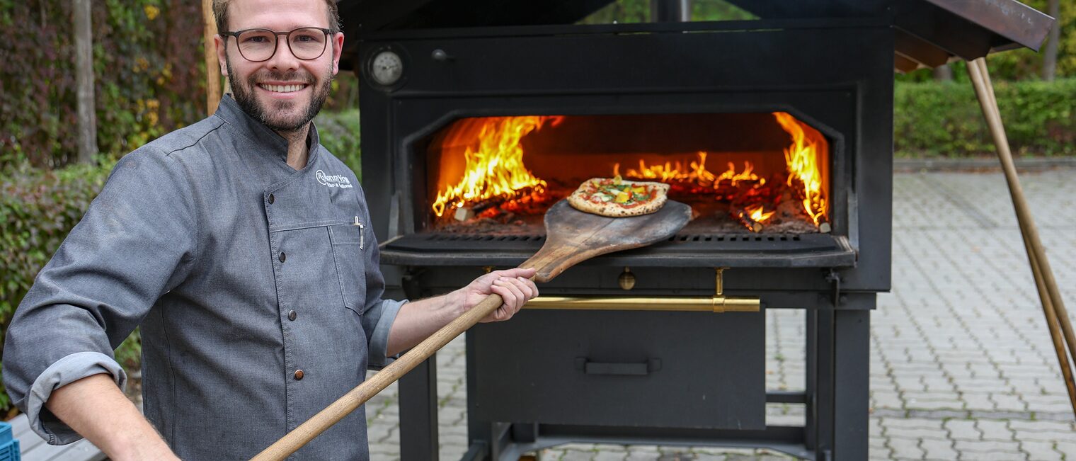 Ausbildungsmeister Ronny Vogel holt eine Pizza aus dem Holzofen.