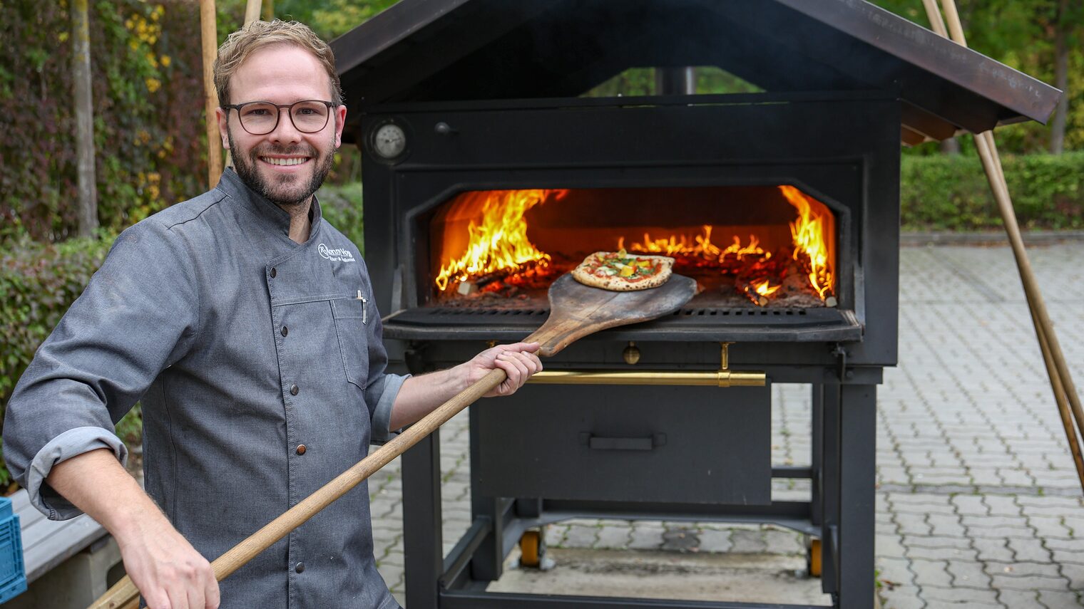 Ausbildungsmeister Ronny Vogel holt eine Pizza aus dem Holzofen.