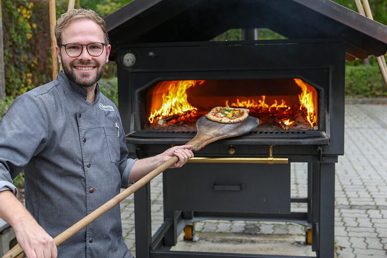 Ausbildungsmeister Ronny Vogel holt eine Pizza aus dem Holzofen.