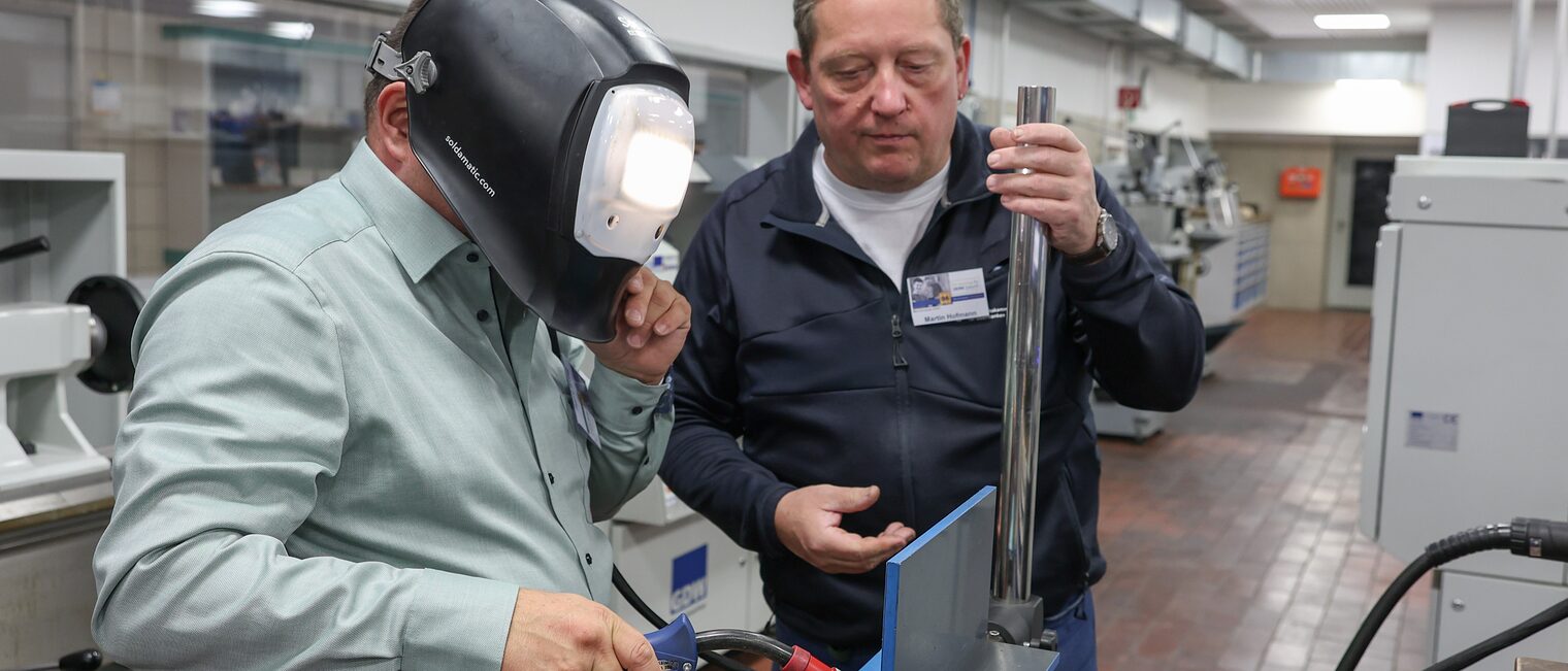 Harald Sattler trägt eine Schweißerbrille und schweißt unter Anleitung digital am Bildschirm.