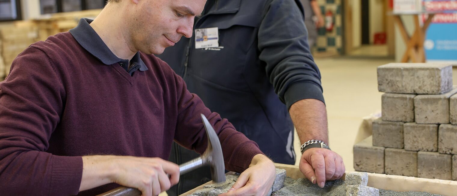 Sebastian Serfas pflastert eine Reihe an Pflastersteinen auf Schotter.