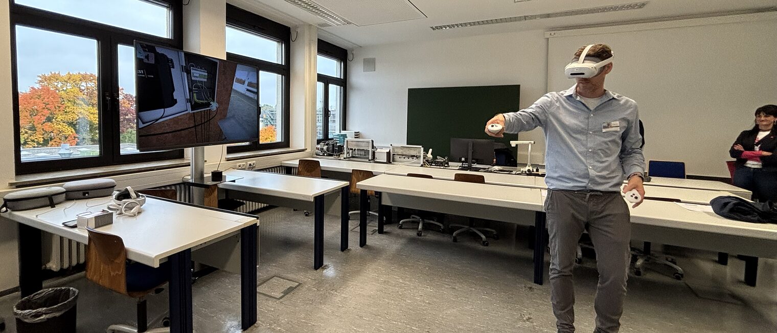 Stefan Kolb trägt eine VR-Brille und zeigt das Verkabeln eines Verteilerkastens am Bildschirm.