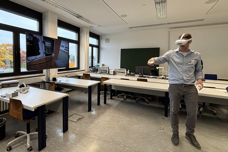 Stefan Kolb trägt eine VR-Brille und zeigt das Verkabeln eines Verteilerkastens am Bildschirm.