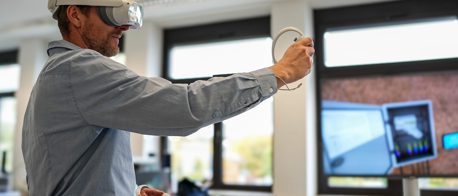 Ein junger Mann trägt eine VR-Brille und hält einen Controller in der Hand.