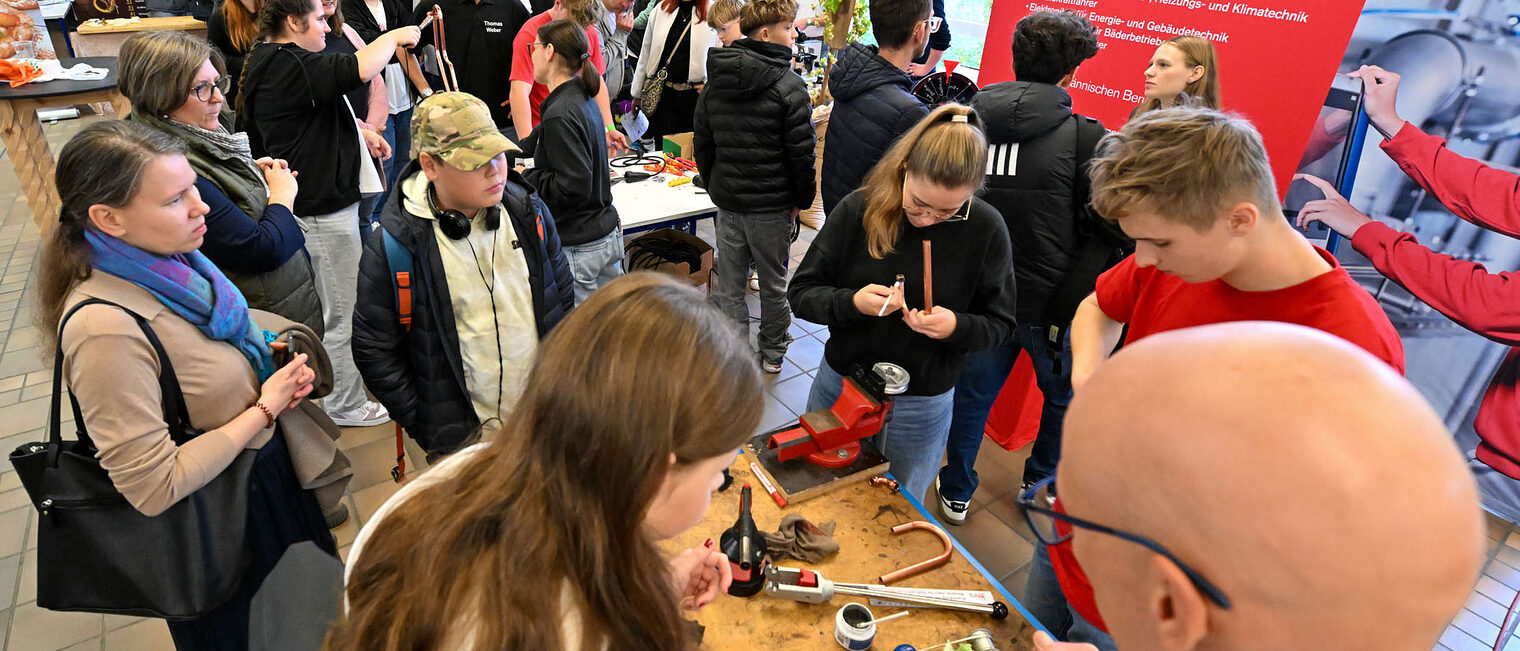 Jugendliche stehen um einen Stand herum und fertigen Metallherzen aus Kupfer.