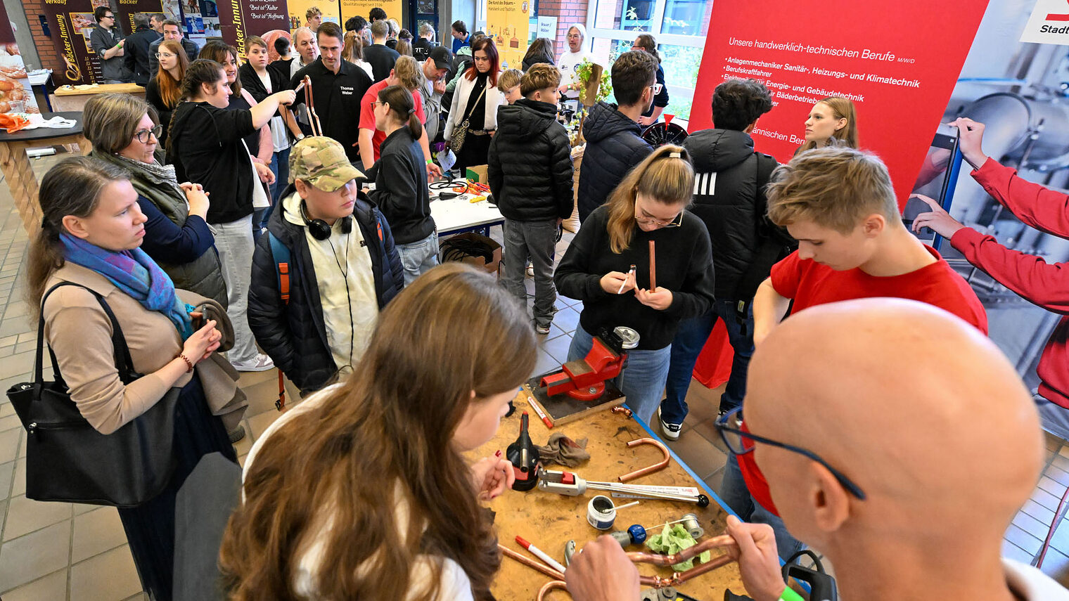 Jugendliche stehen um einen Stand herum und fertigen Metallherzen aus Kupfer.