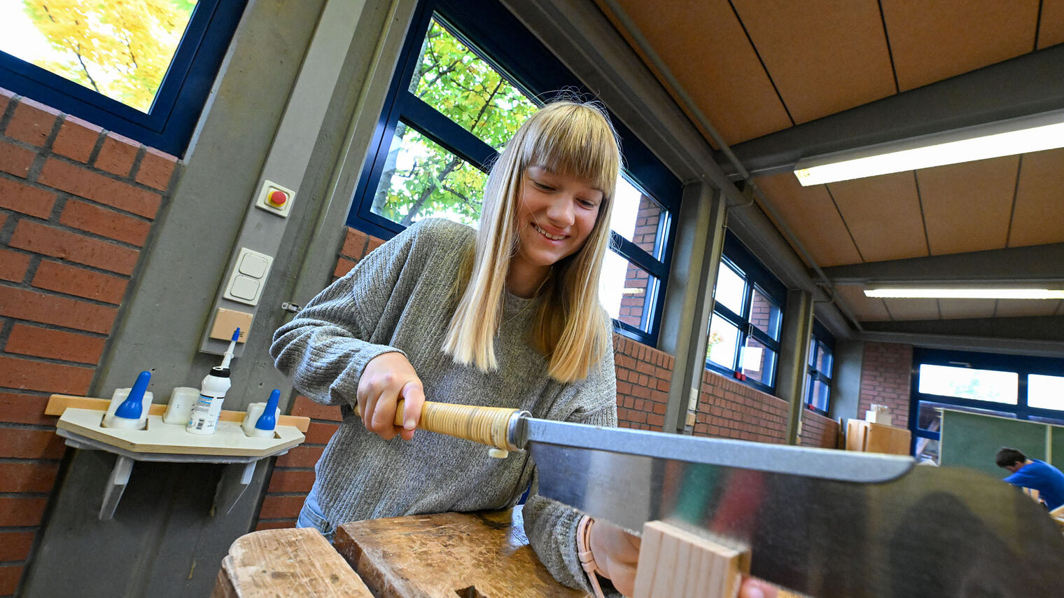 Eine Jugendliche sägt mit einem Schwertähnlichen Gegenstand ein Holzstück.