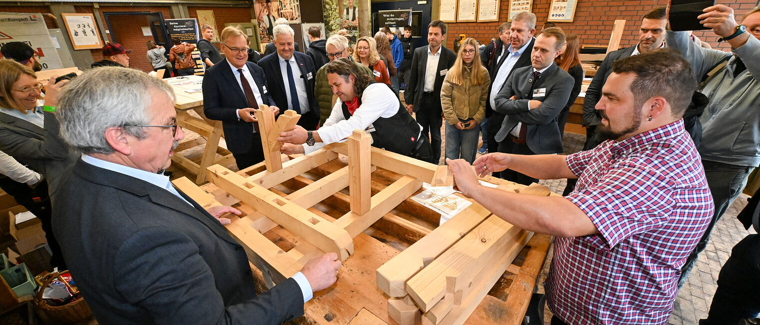 Die Ehrengäste sehen zu, wie eine Holzkonstruktion zusammengebaut wird.
