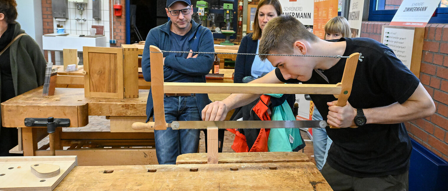 Ein Jugendlicher sägt unter Aufsicht mit einer Holzsäge. 