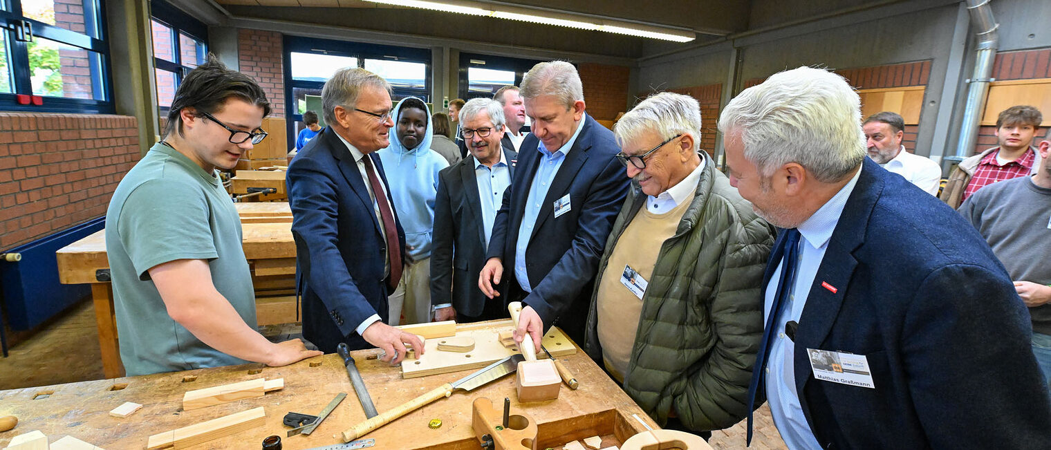 Die Ehrengäste der Berufsmesse sehen sich eine Werkbank mit Werkzeugen an, mit denen man Holz bearbeitet.