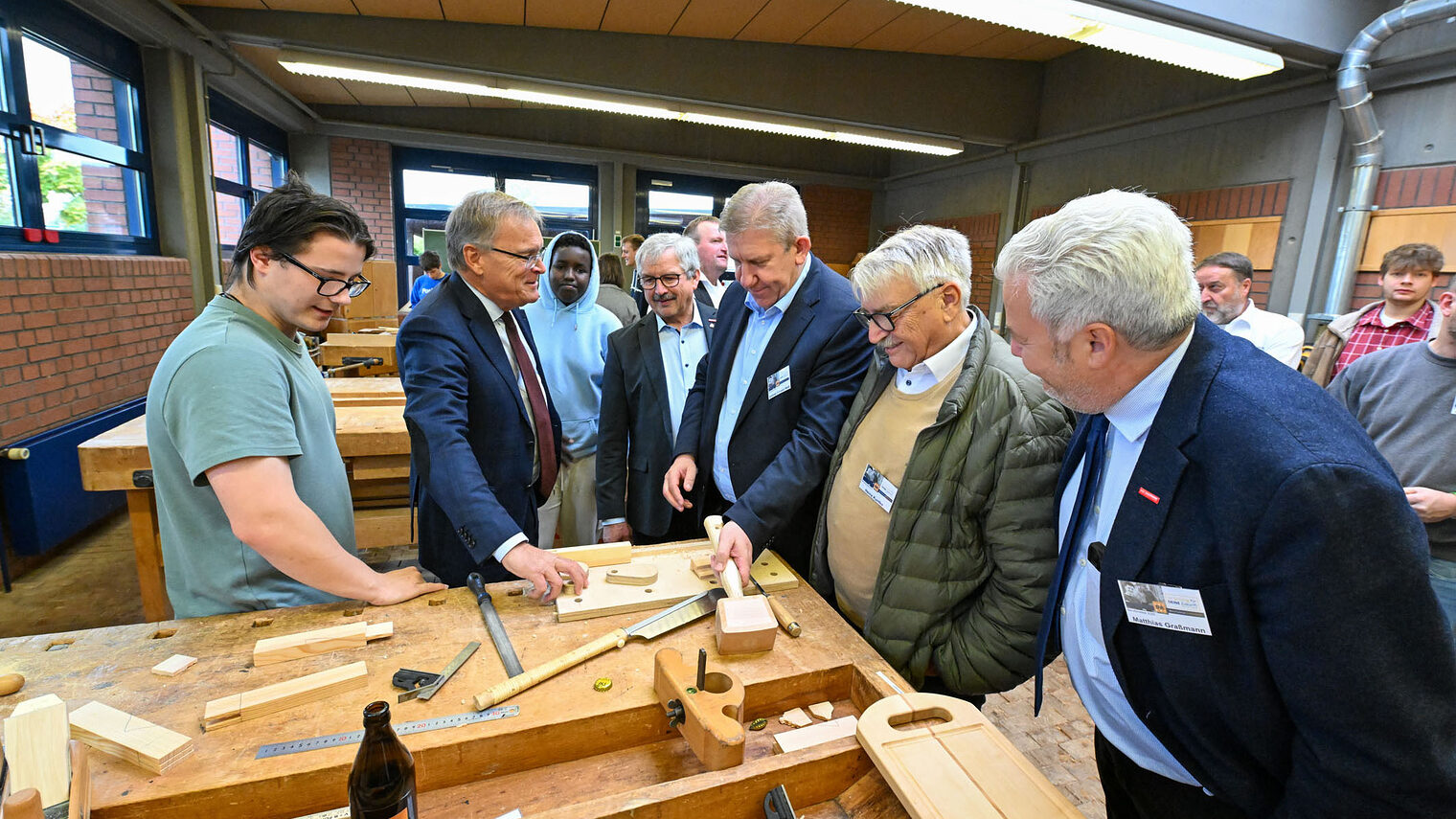 Die Ehrengäste der Berufsmesse sehen sich eine Werkbank mit Werkzeugen an, mit denen man Holz bearbeitet.