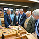 Die Ehrengäste der Berufsmesse sehen sich eine Werkbank mit Werkzeugen an, mit denen man Holz bearbeitet.