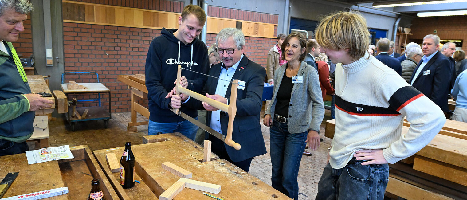 Wolfgang Ammon bedient eine Holzsäge während andere Menschen zusehen.