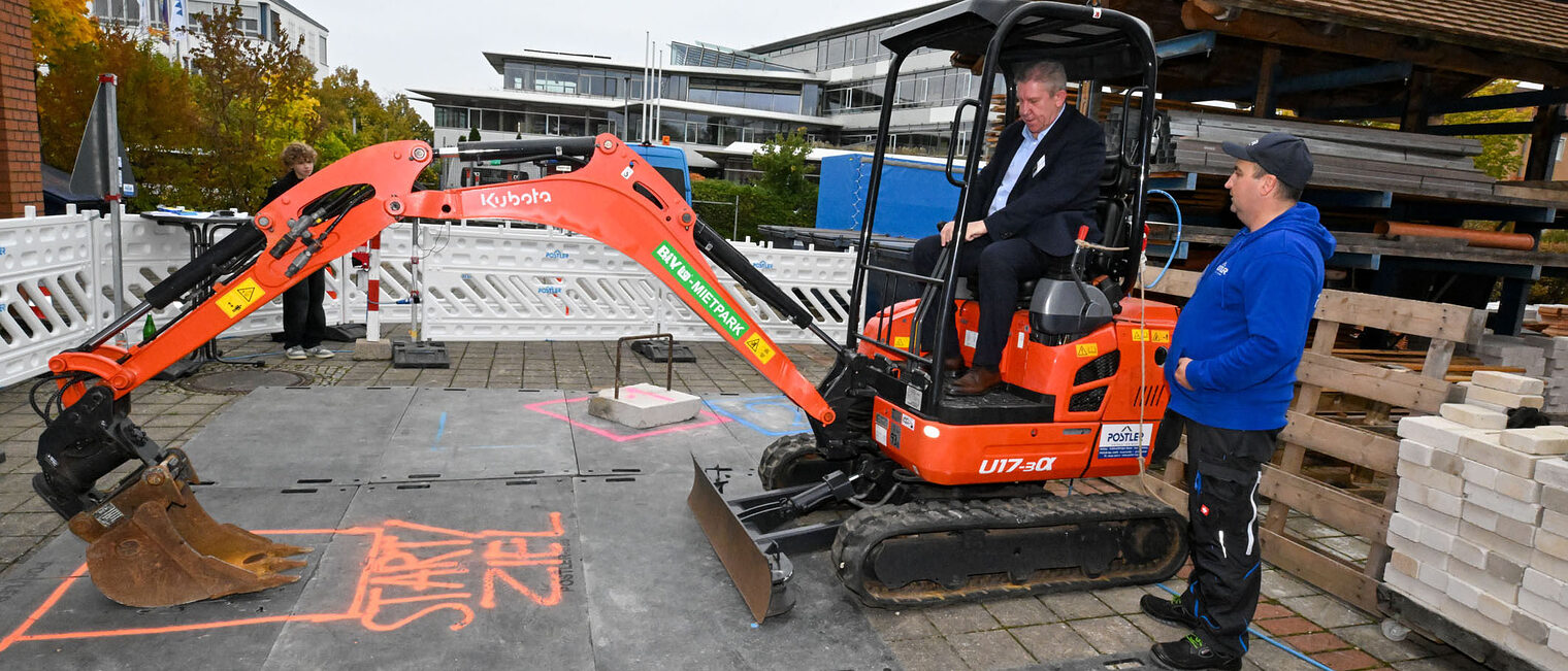 Ein Mann fährt unter Anleitung mit einem Bagger und bedient die Schaufel.