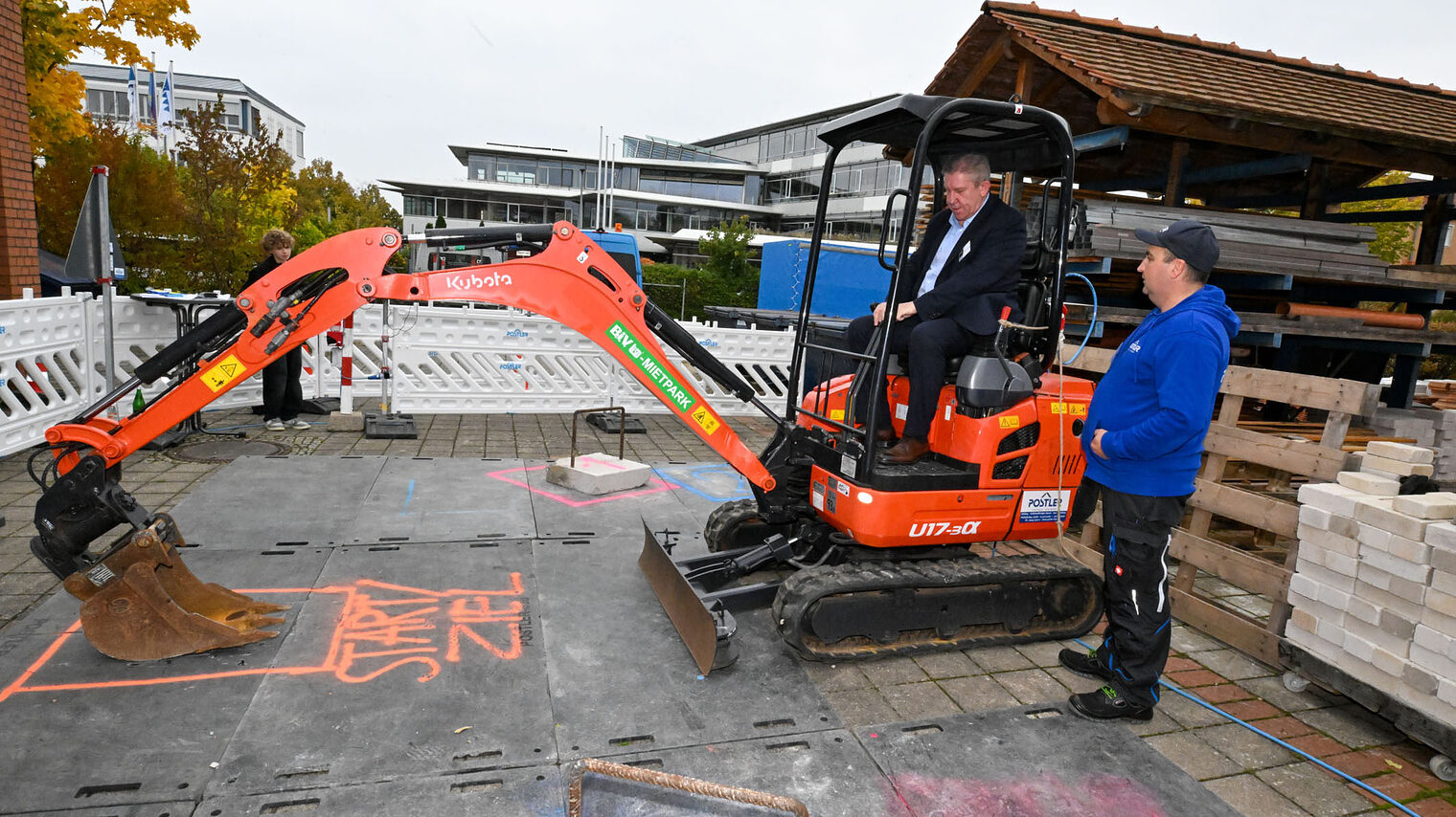 Ein Mann fährt unter Anleitung mit einem Bagger und bedient die Schaufel.