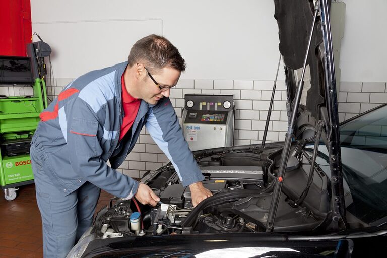 Ein Kraftfahrzeugmechatroniker schraubt am Motor eines Autos herum.