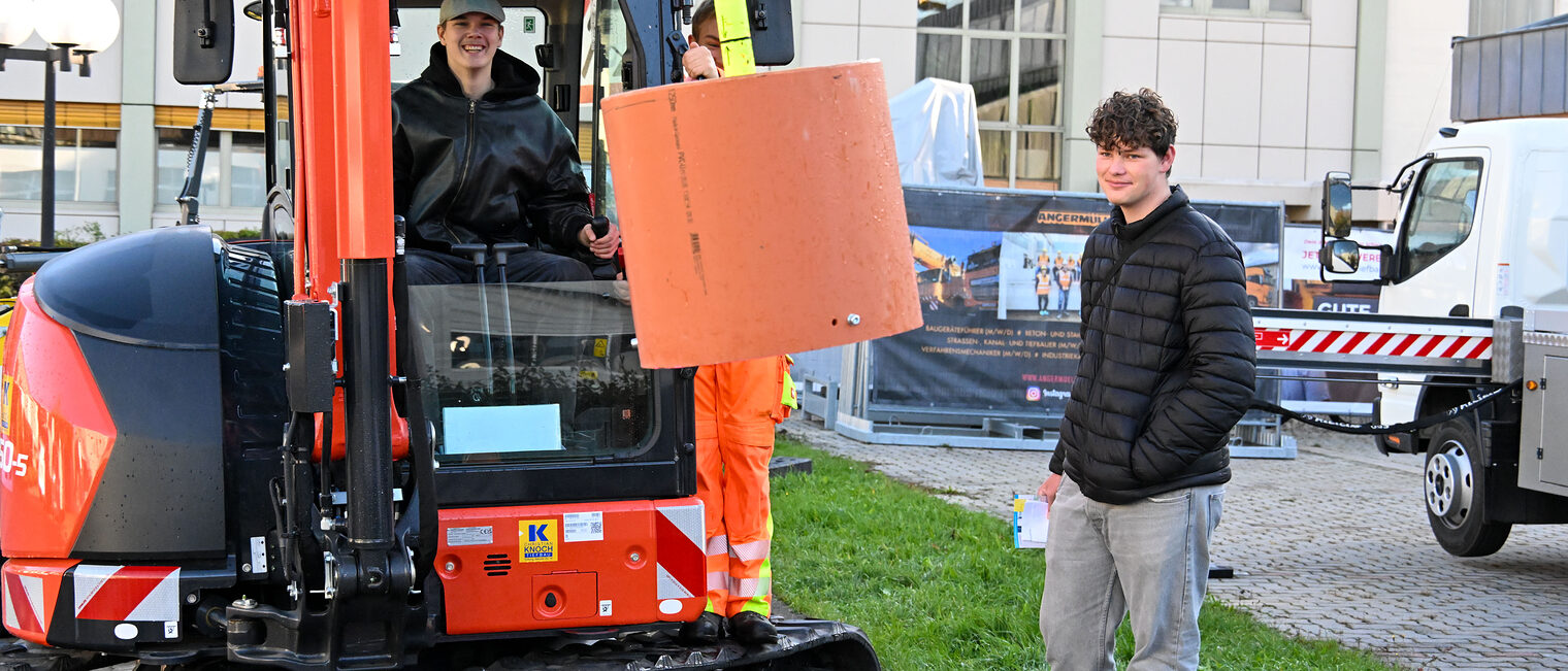 Ein Jugendlicher steuert einen Bagger während ihm ein anderer Jugendlicher dabei zusieht.