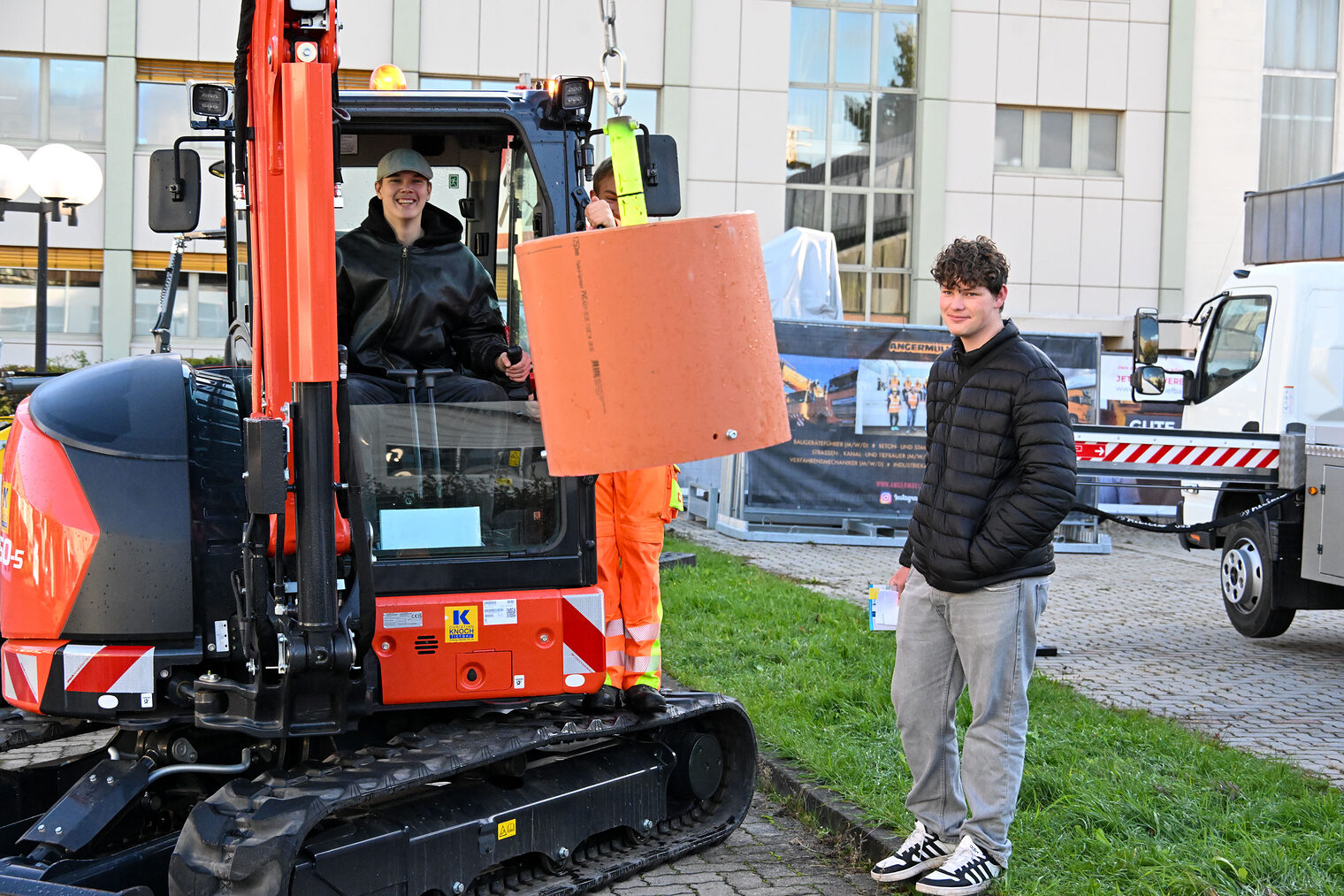 Ein Jugendlicher steuert einen Bagger während ihm ein anderer Jugendlicher dabei zusieht.