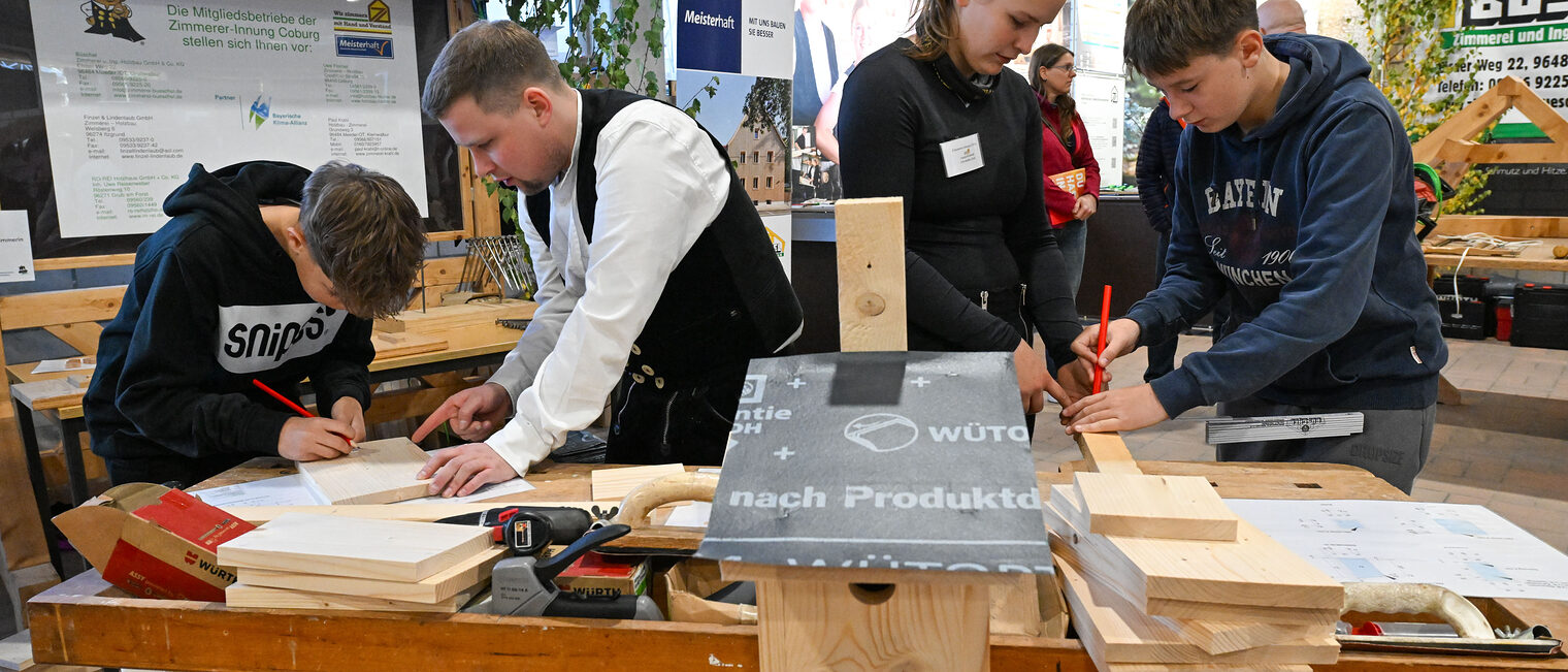 Jugendliche zeichnen unter Aufsicht mit Bleistiften Holzstücke an.