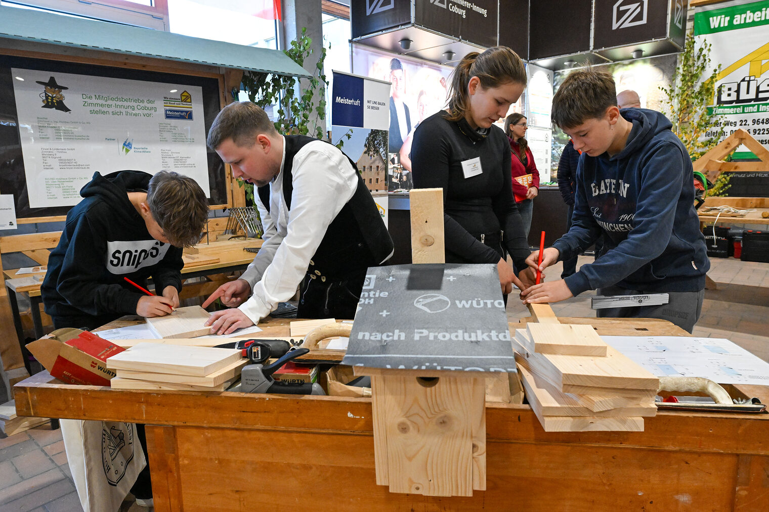 Jugendliche zeichnen unter Aufsicht mit Bleistiften Holzstücke an.