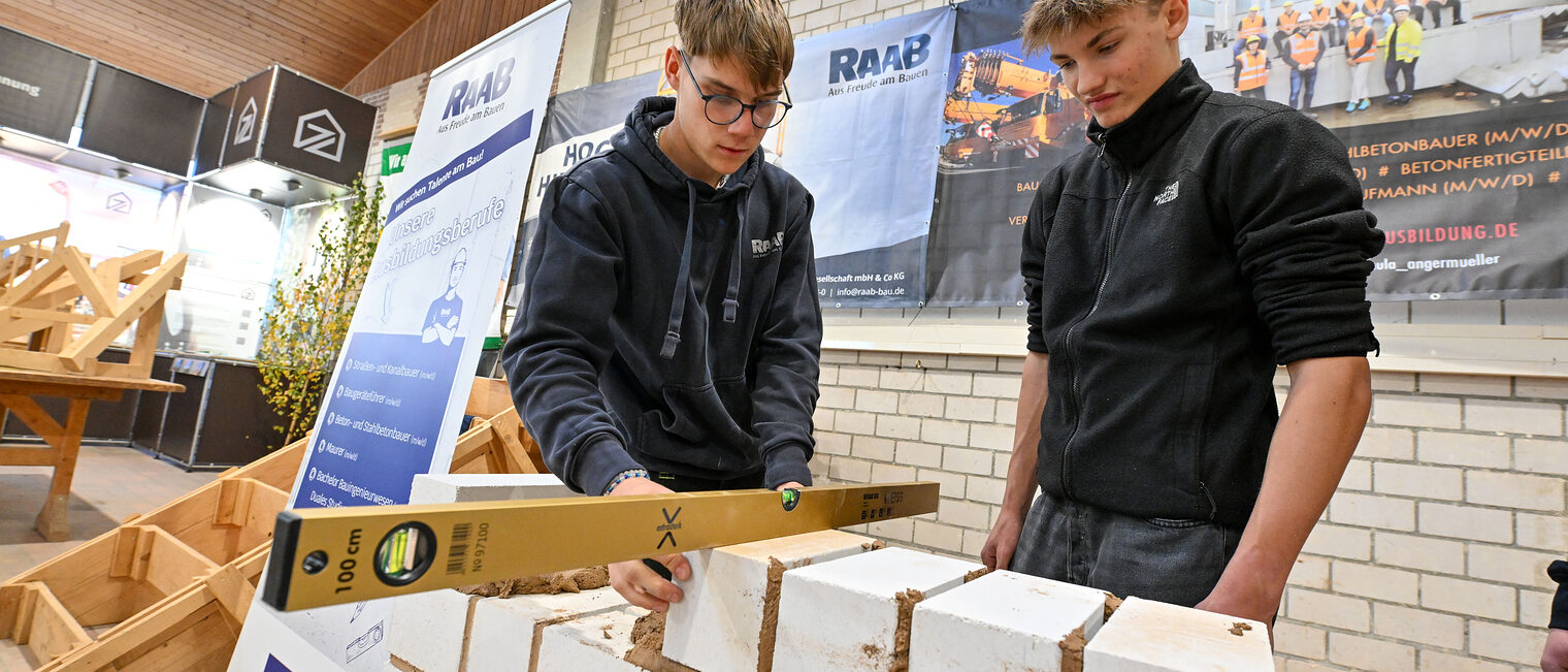 Zwei Jugendliche prüfen mit einer Wasserwaage, ob die Steine auf der Mauer gerade sitzen.