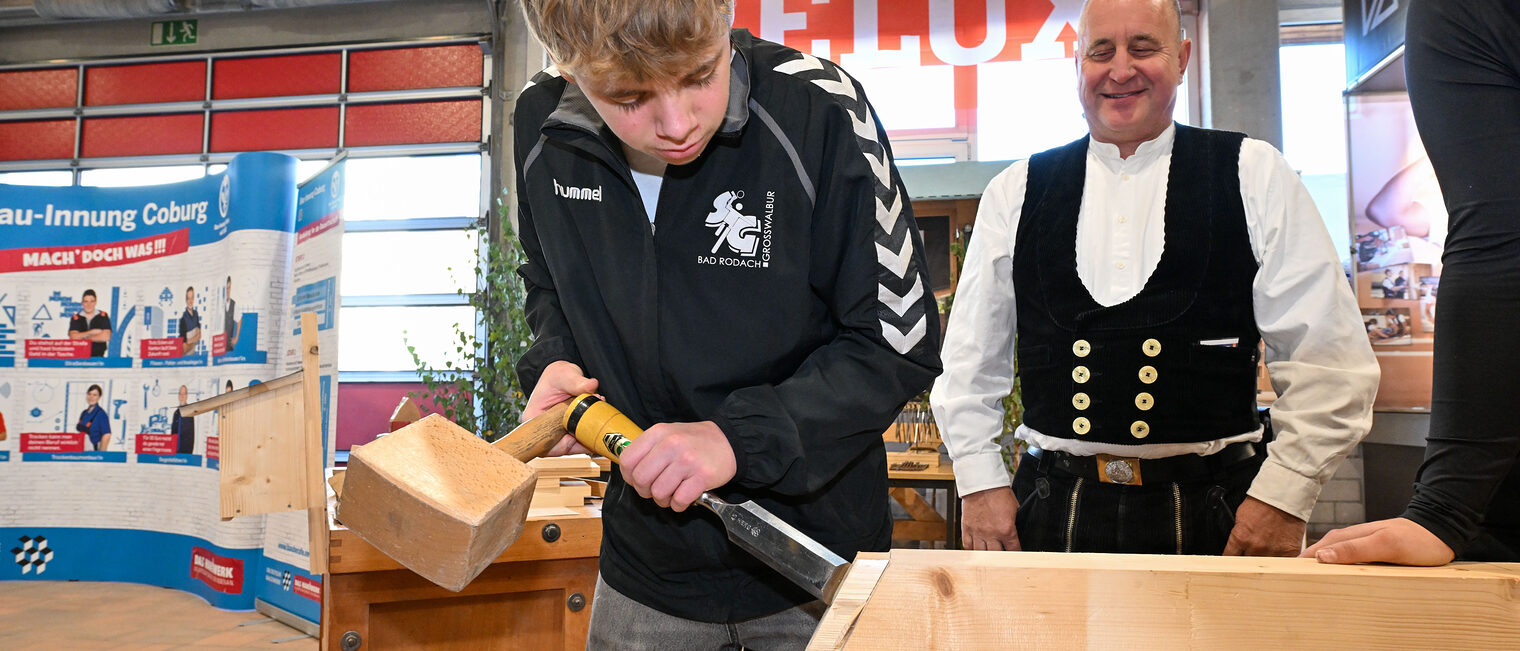 Ein Jugendlicher bearbeitet einen Holzbalken mit Stößel und Meißel.