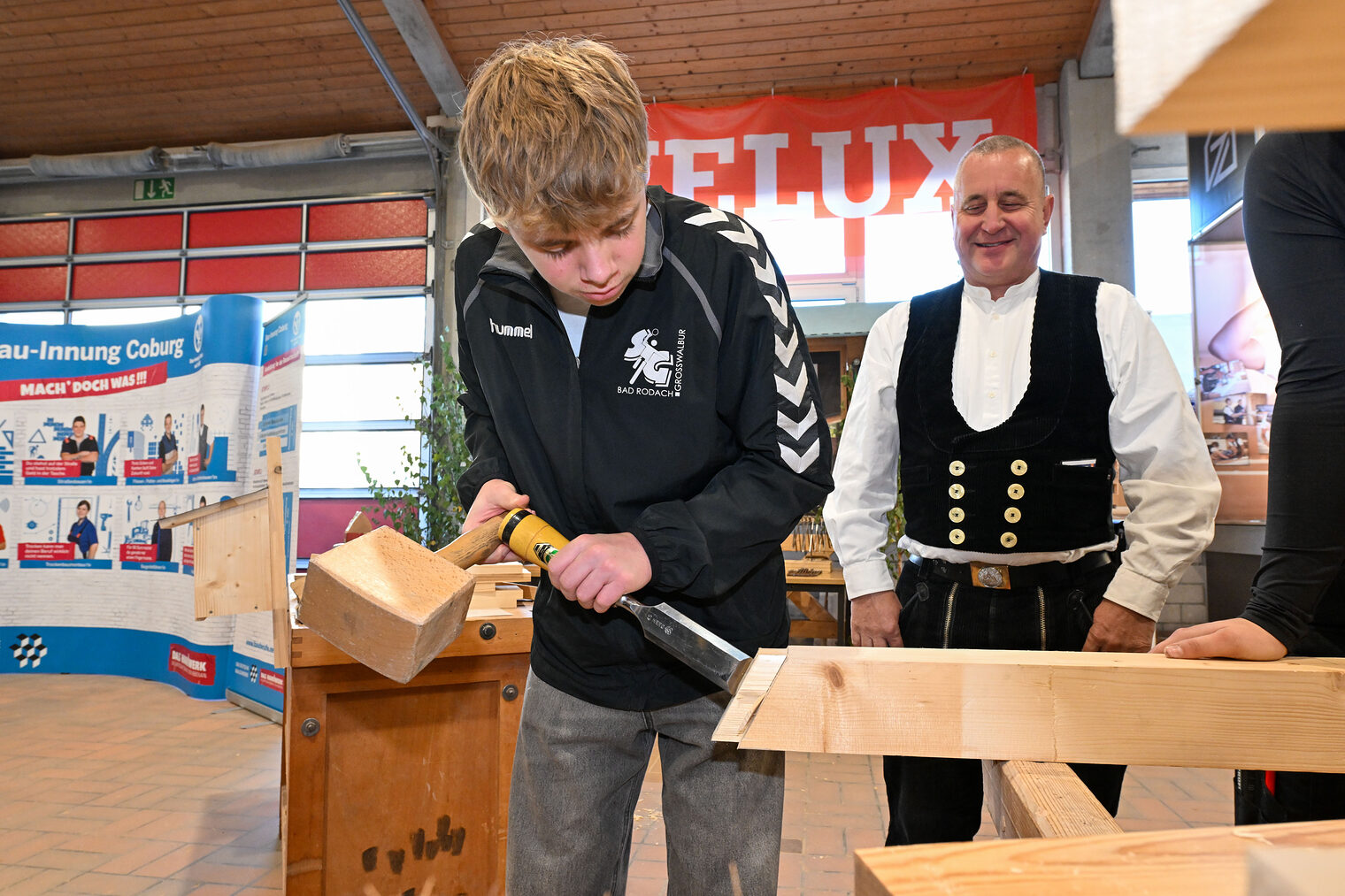 Ein Jugendlicher bearbeitet einen Holzbalken mit Stößel und Meißel.