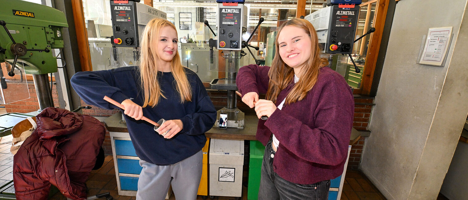 Zwei Jugendliche säubern lächelnd Metallrohre.