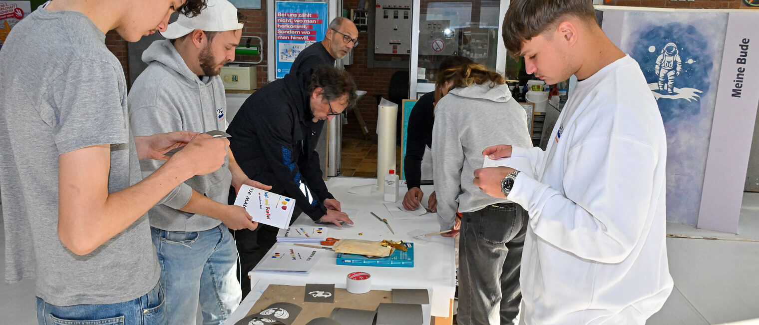 Eine Gruppe von Jugendlichen betrachtet Schablonen für die Fahrzeuglackierung.