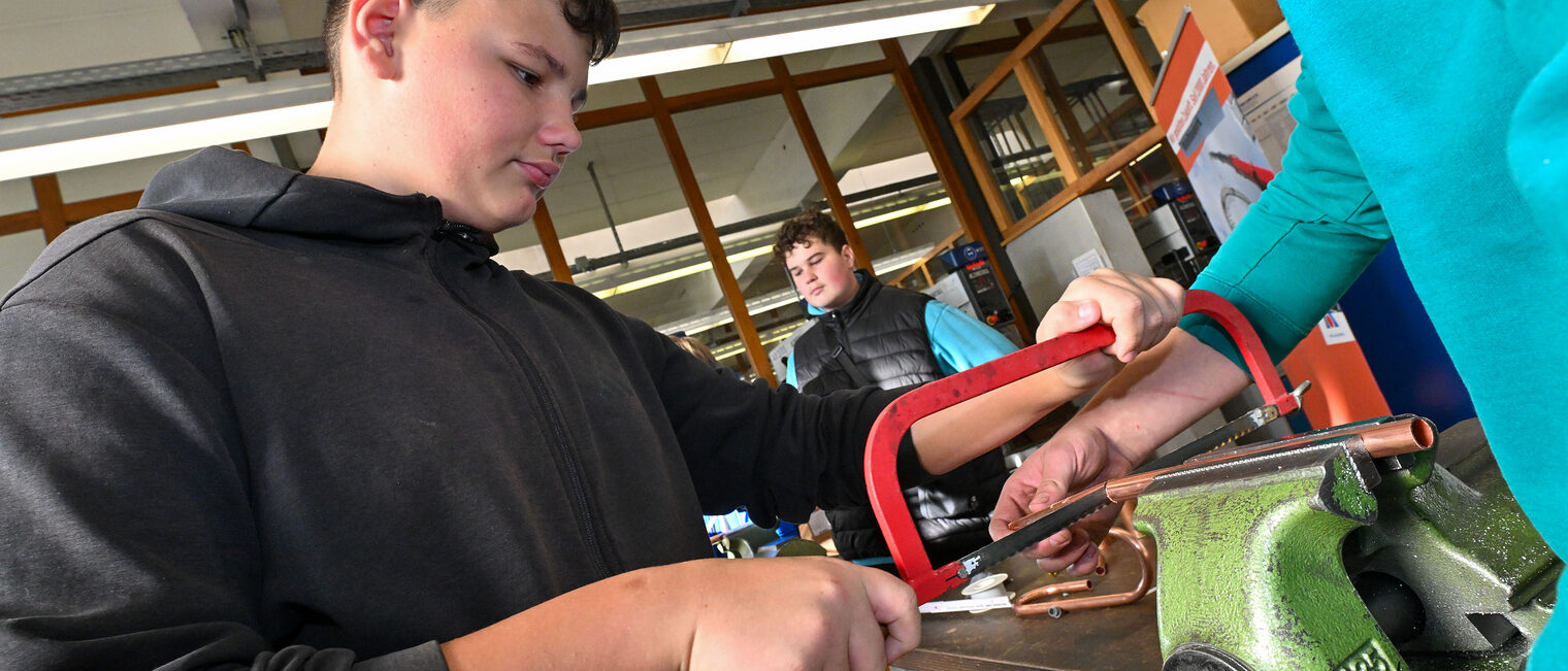 Ein Jugendlicher sägt ein Metallrohr ab.