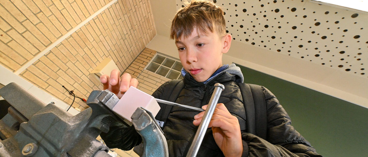 Ein Jugendlicher feilt einen Metallwürfel in einem Schraubstock zurecht.