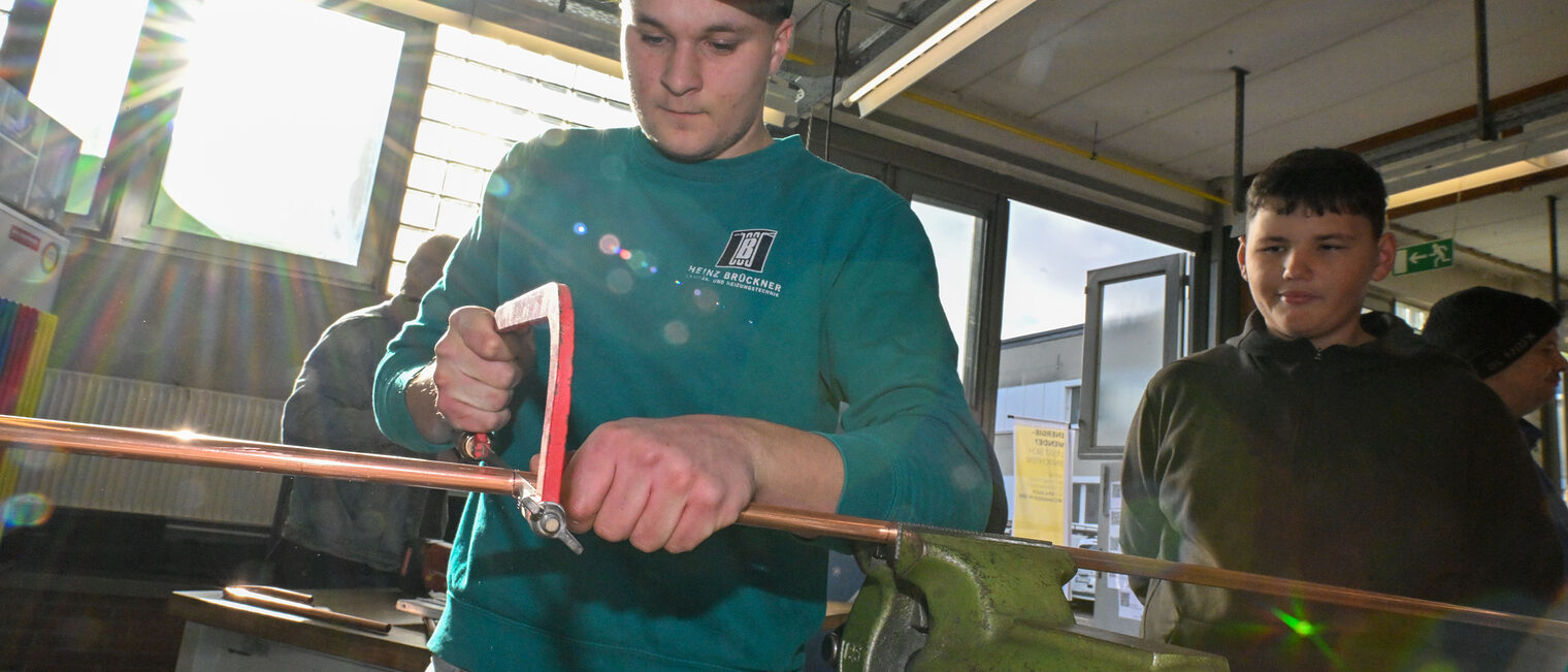 Ein Jugendlicher sägt unter Beaufsichtigung ein Metallrohr zurecht.