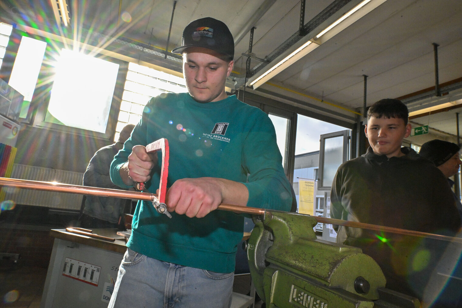Ein Jugendlicher sägt unter Beaufsichtigung ein Metallrohr zurecht.