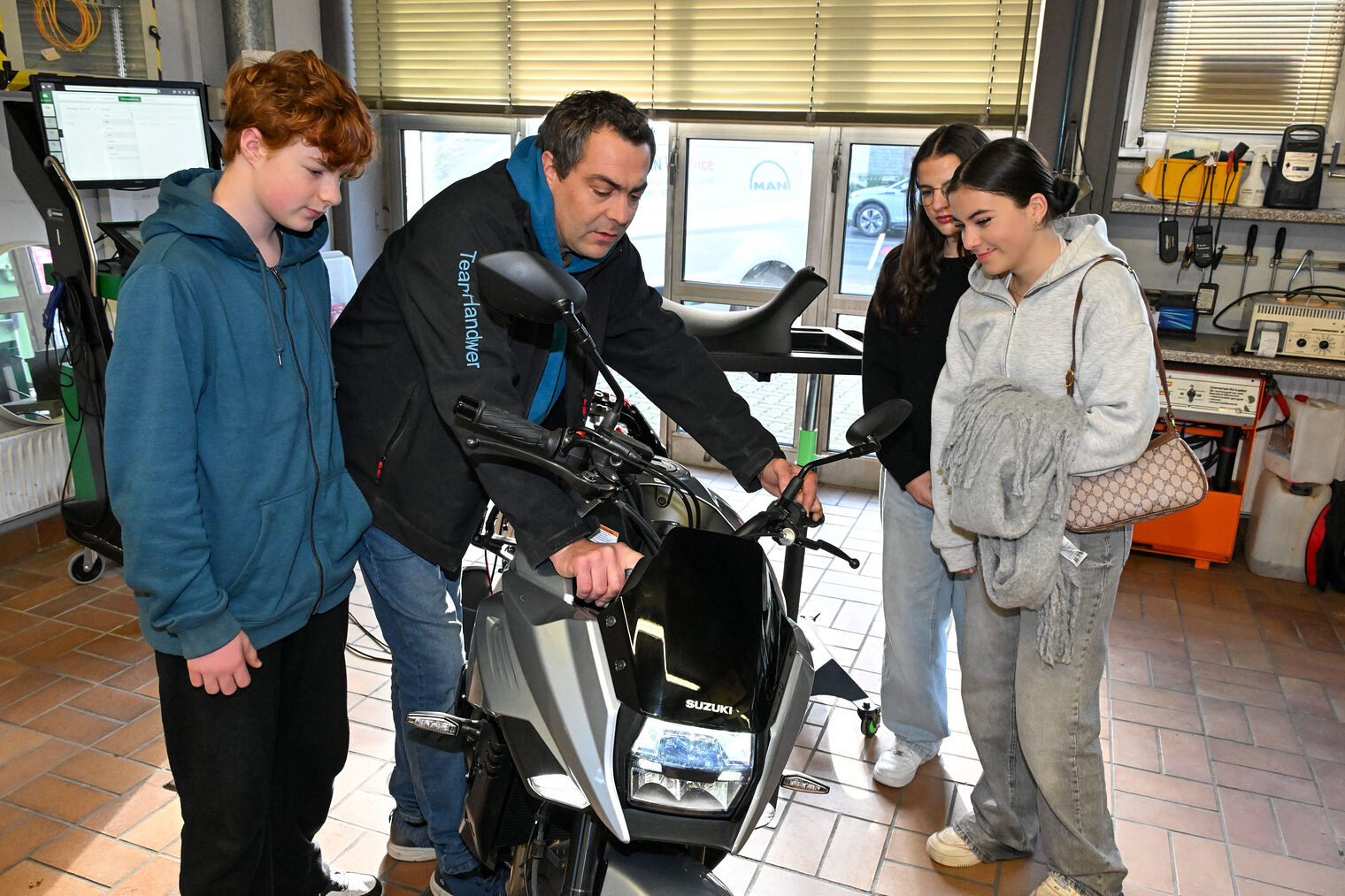Ein Ausbilder zeigt drei Jugendlichen, wie sie ein Motorrad reparieren. 