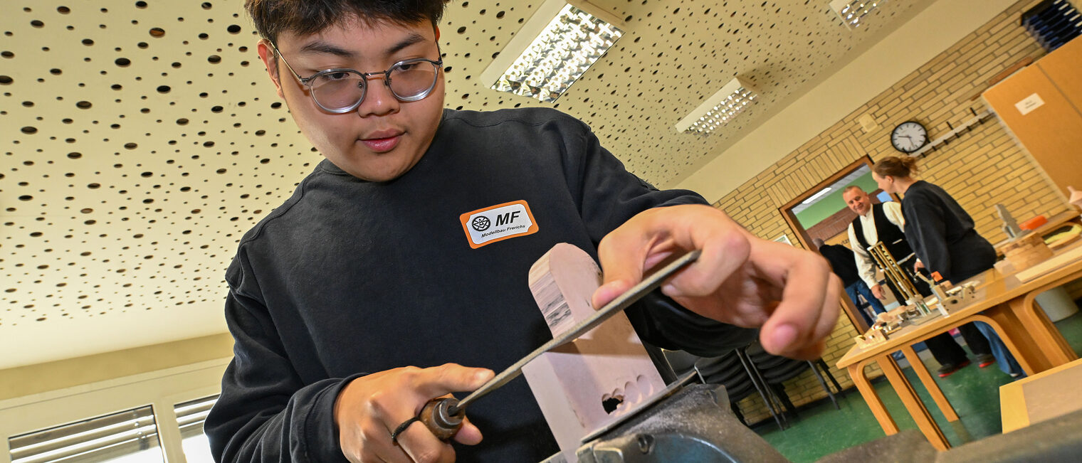 Ein Jugendlicher feilt ein Metallstück in einem Schraubstock zurecht.