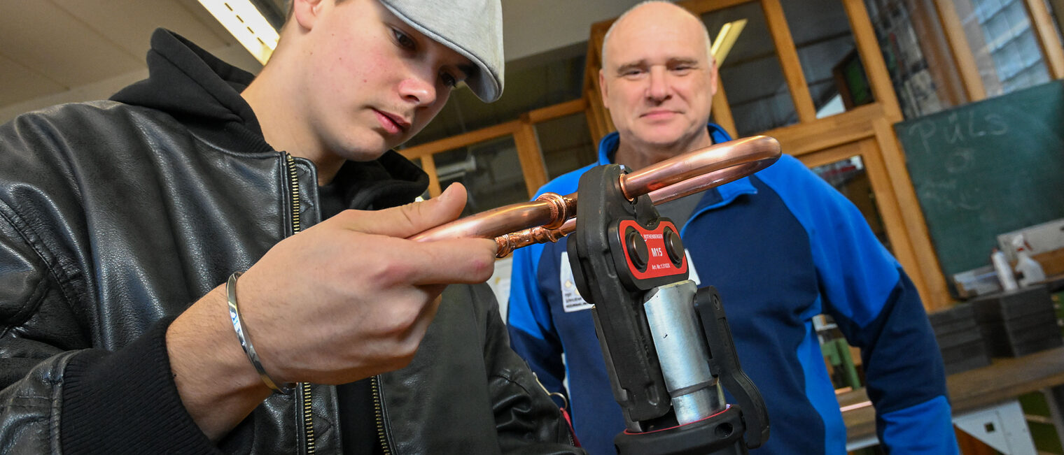 Ein Jugendlicher biegt unter Aufsicht ein Herz zurecht.